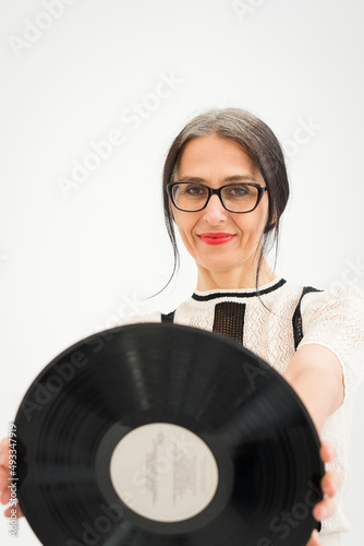 Studio photo of middle aged woman starting getting grey-haired wearing black and white clothes with vinyl record in hands on white background, middle age sexy lady, happy life concept