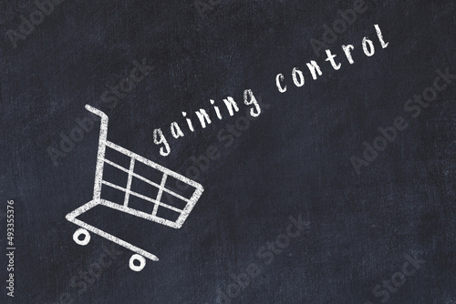 Chalk drawing of shopping cart and word gaining control on black chalboard. Concept of globalization and mass consuming photo