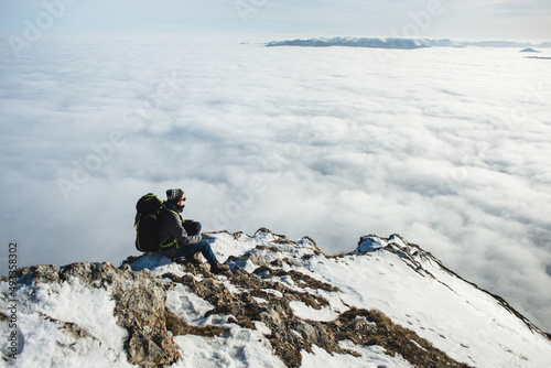 Adult male hiker sitting on rocky mountain above clouds  photo