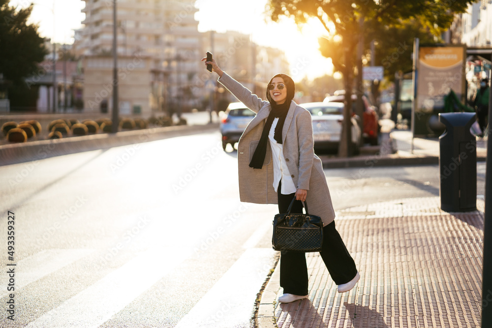 Smiling Muslim woman catching taxi on sidewalk Smiling Muslim woman catching taxi on sidewalk