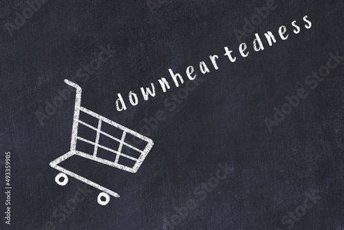 Chalk drawing of shopping cart and word downheartedness on black chalboard. Concept of globalization and mass consuming photo