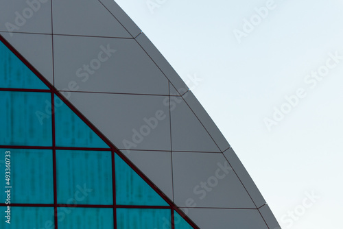 The exterior wall of a contemporary commercial style building with aluminum metal composite panels and glass windows. The futuristic building has engineered diagonal cladding steel frame panels. © Dolores Harvey