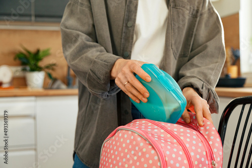 Crop woman packing lunch box in backpack