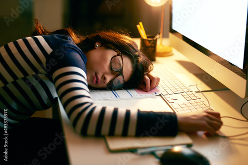 When you just cant keep your eyes open any longer. Shot of a young businesswoman sleeping on her desk while working late in an office.
