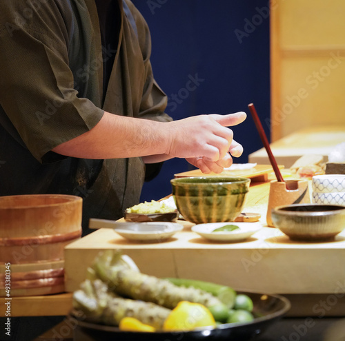 Chef in black uniform making nigiri sushi at sushi bar.