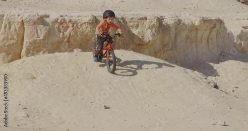 Slow motion shot of a young, blonde boy in helmet riding a bike on a desert. photo