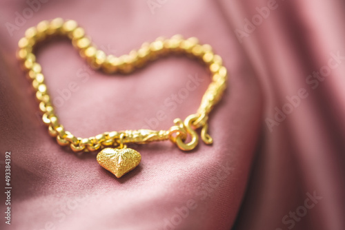 The gold bracelet has a heart pendant placed on a pink gold fabric.