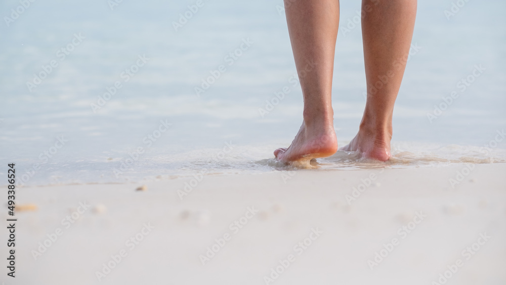 Closeup image of woman with barefoot while walking on the white beach and the sea Closeup image of woman with barefoot while walking on the white beach and the sea