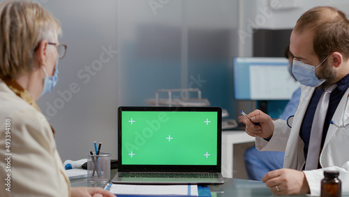 Elder person looking at greenscreen on laptop at checkup visit with medic during pandemic. Senior patient and doctor analyzing mockup copyspace with isolated chromakey template at examination.