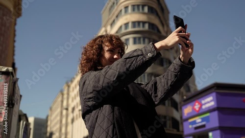 Curly Caucasian Woman Taking Selfie With Smartphone In City Center photo