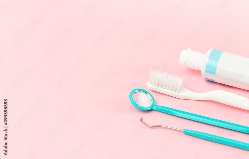 dental instruments, toothbrush and paste on pink background