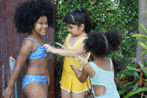 Two African girls and an Asian girl in swimsuits splashing around using a rubber hose before entering the pool and having fun in the garden. photo