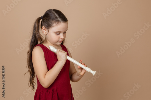 Φωτογραφία Girl in red dress hold common flute with head down and clamp holes on it, beige background