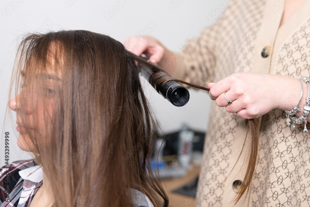 Fototapeta premium The stylist curls the girl's hair with a curling iron