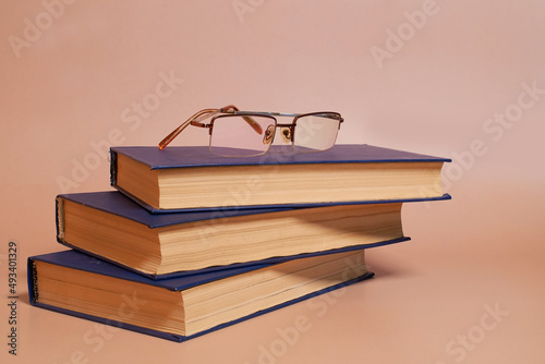 Reading glasses are on a stack of books on a colored background. Side view