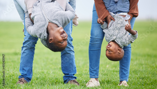 Do anything, but let it produce joy. Shot of two children hanging upside down by their parents outside.