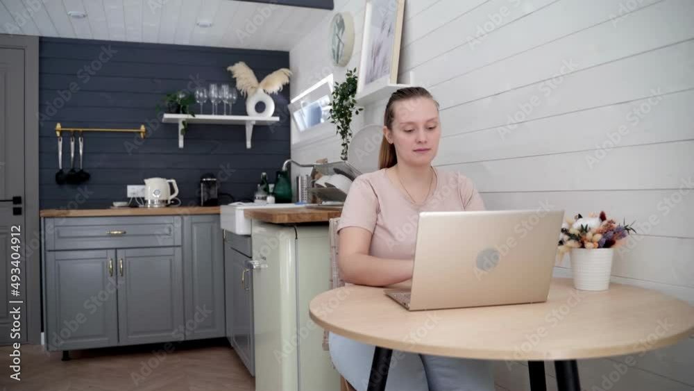 Woman is working on laptop, sitting at the kitchen table at home. Freelancer, remote work, work in pandemic Woman is working on laptop, sitting at the kitchen table at home. Freelancer, remote work, work in pandemic