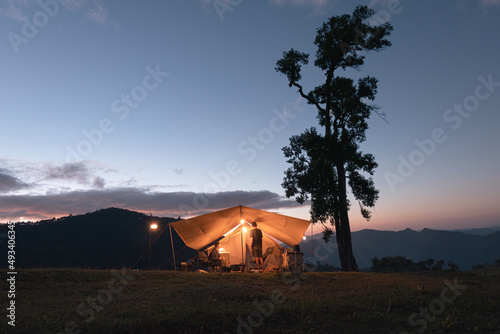 Group of friends camping with lamp shine and large tree on hill in national park