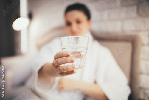 Young woman drinking clear water in the morning in her bedroom. Healthy morning rituals.