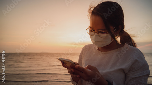 Young Asian woman using smartphone at the beach with sunset skybackground. technology and bussiness concept background.