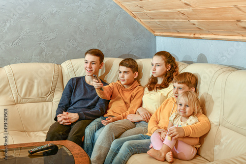 Friendly children watch TV while sitting on a leather sofa in the evening.