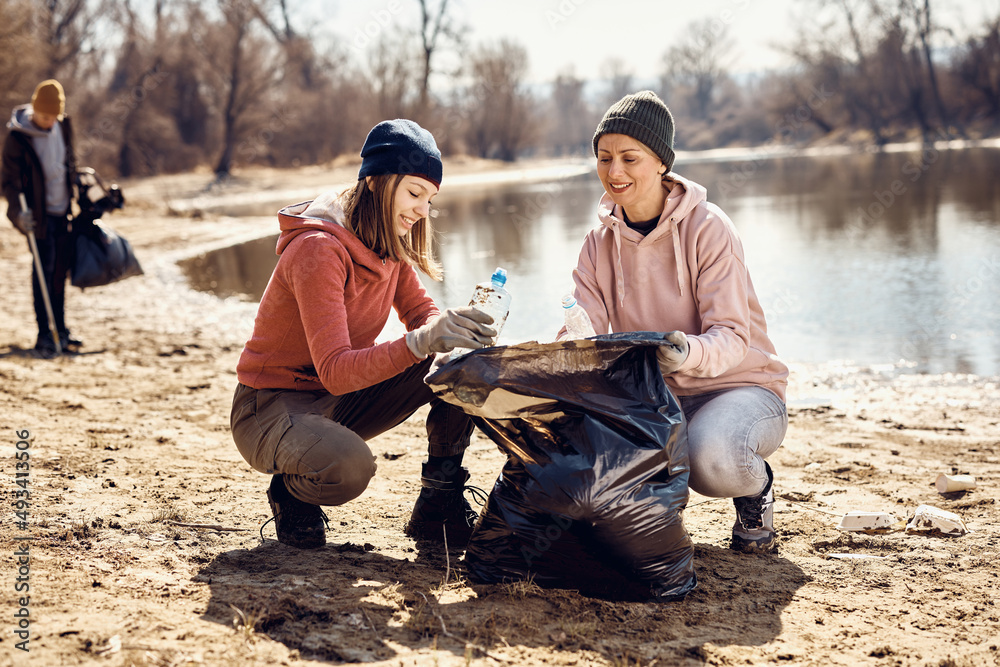 Smiling eco-friendly volunteers picking up garbage together on beach. Smiling eco-friendly volunteers picking up garbage together on beach.