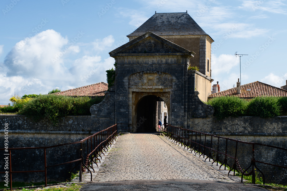 porte des campani in Saint-Martin-de-Ré on Ile de Ré on a sunny day in summertime with people riding on a bike under it.