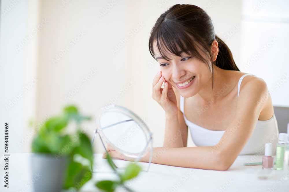 鏡の前で頬に手をあてスキンケアをする女性