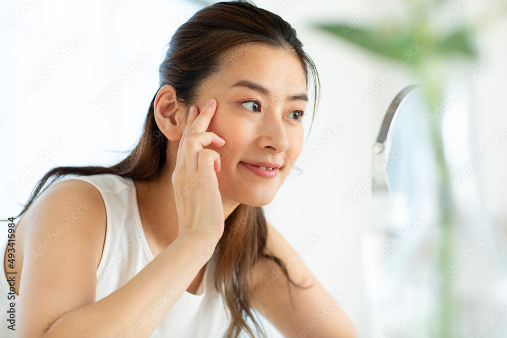 鏡の前で頬に手をあてスキンケアをする女性