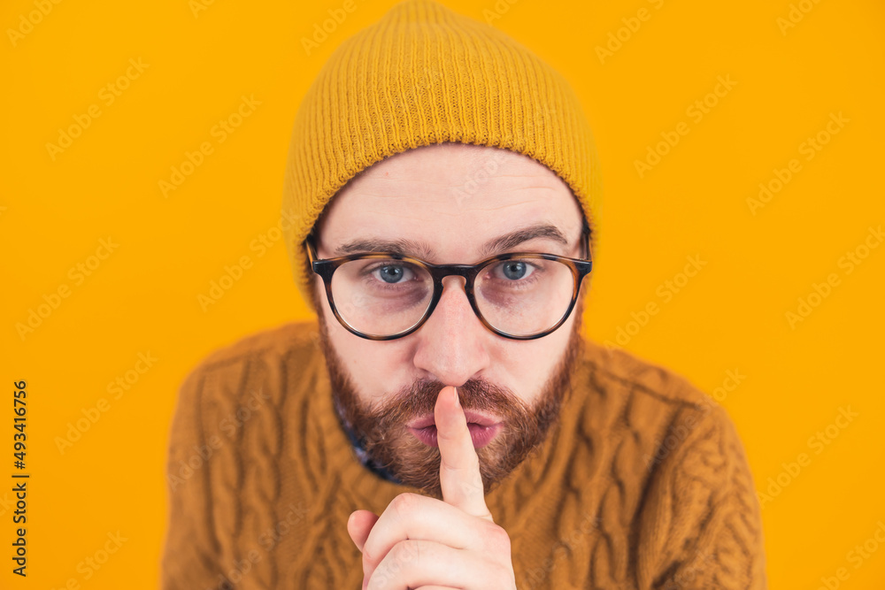 Closeup of young bearded Caucasian man looking at the camera showing hush shh gesture isolated orange background focus on the head . High quality photo Closeup of young bearded Caucasian man looking at the camera showing hush shh gesture isolated orange background focus on the head . High quality photo