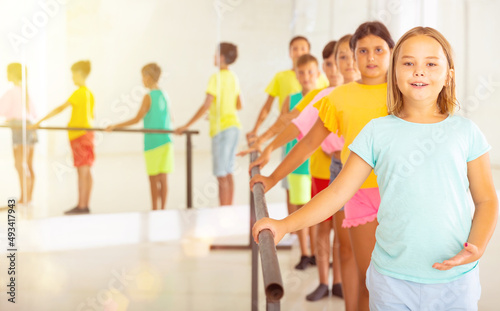 Smiling tween girl practicing classic dance moves near ballet barre during group class.