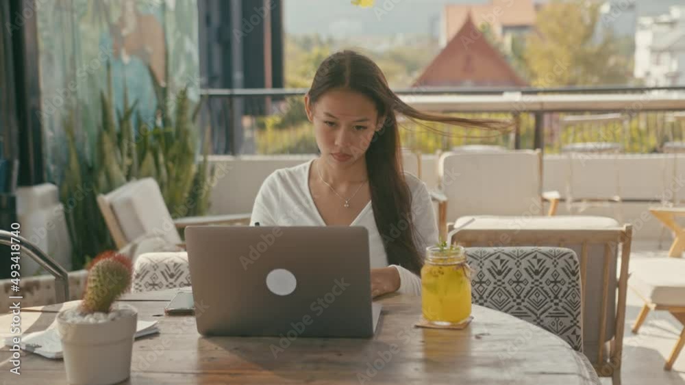 A young Asian girl works at her laptop in a rooftop cafe in the city A young Asian girl works at her laptop in a rooftop cafe in the city