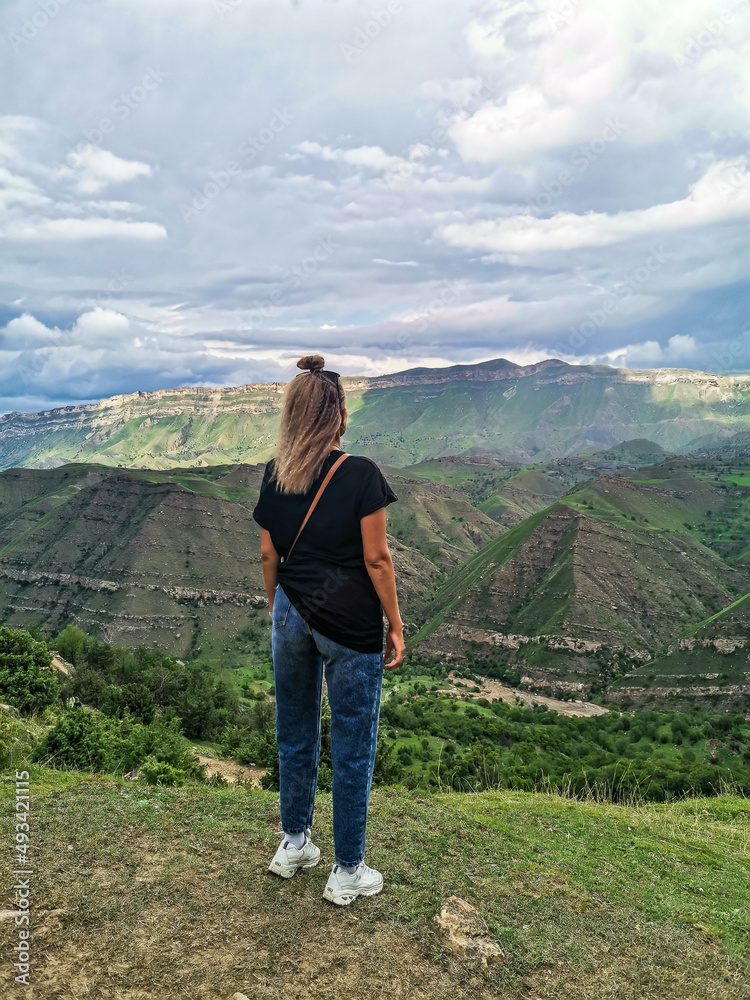 A girl on the background of the village of Kurib in the Caucasus mountains, on top of a cliff. Dagestan Russia June 2021