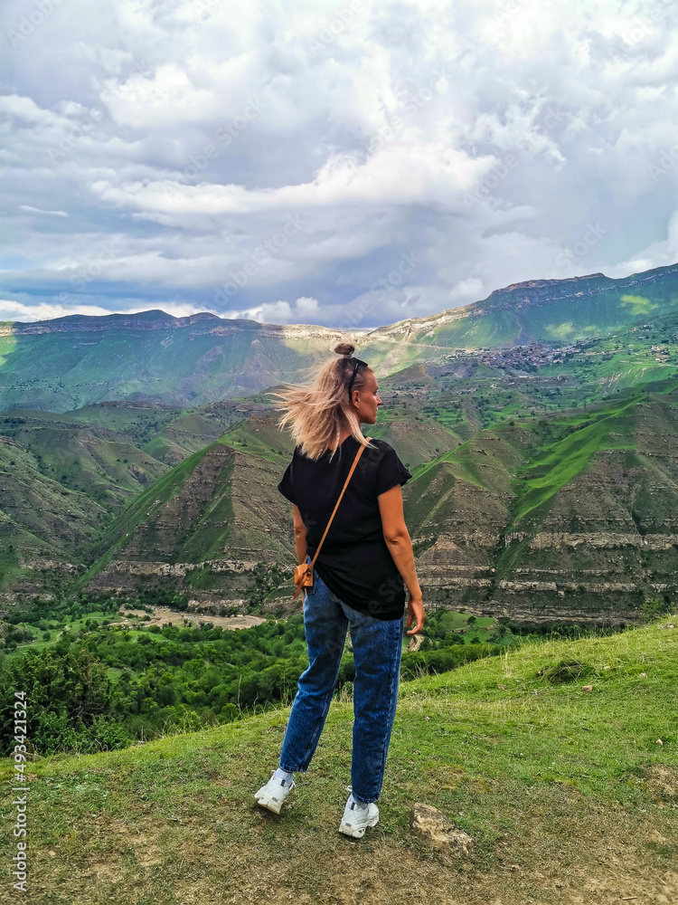A girl on the background of the village of Kurib in the Caucasus mountains, on top of a cliff. Dagestan Russia June 2021