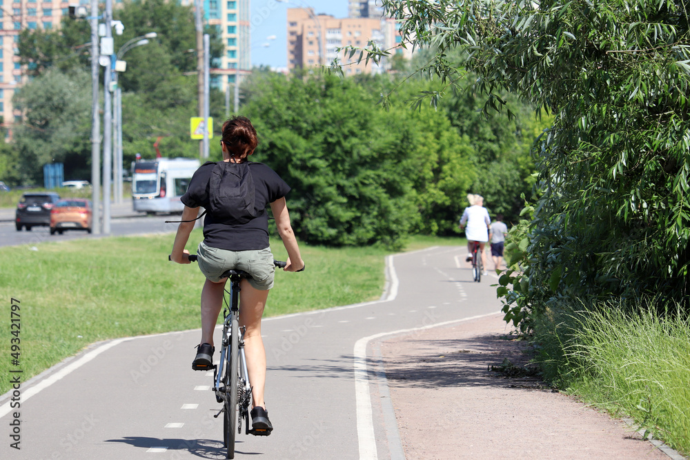 Girl in shorts riding on a bicycle on a path in a green city park. Woman cyclist, spring or summer leisure, cycling concept