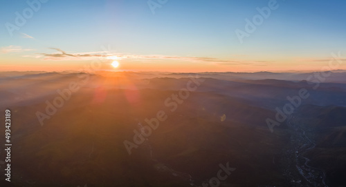 Fototapeta Naklejka Na Ścianę i Meble -  Aerial view of dark mountain hills with bright sunrays of setting sun at sunset. Hazy peaks and misty valleys in evening