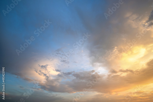 Dramatic cloudy sunset landscape with puffy clouds lit by orange setting sun and blue sky