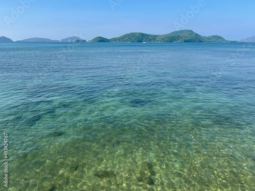 Amazing beautiful transparent turquoise water. View from the calm sea to the land. Sailboats at the distance at the horizon. Tropical paradise. Summer season. Panorama, seascape. Navigational, ocean.