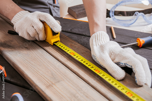 Carpenter is measuring length of wood planks or timbers by measuring tape or ruler. Carpenter workspace, craftsman entrepreneur. photo