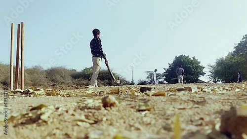 Children enjoying various sports on the playground,a young boy batting hits the cricket ball for a six in a open field in an Indian village,