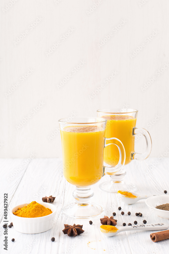 Golden turmeric latte in glasses, spices and cinnamon on white wooden background. Golden turmeric latte in glasses, spices and cinnamon on white wooden background.