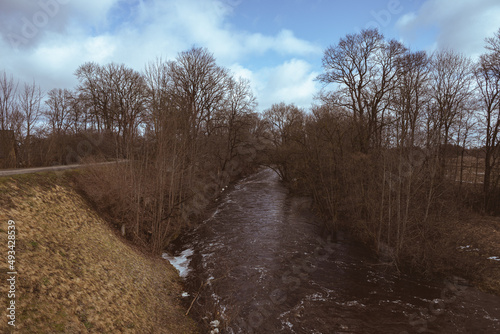 rapid river in valley, bare trees, walkway on riverside 