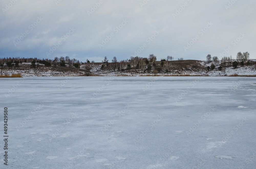 Frozen lake in winter in cloudy weather. Lake surrounded by hills