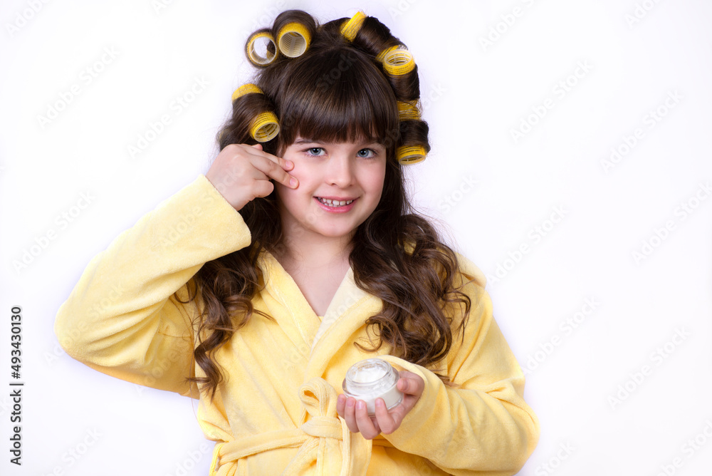 Little and beautiful girl holds vial it in her hand and applying moisturizer cream on her face Little and beautiful girl holds vial it in her hand and applying moisturizer cream on her face
