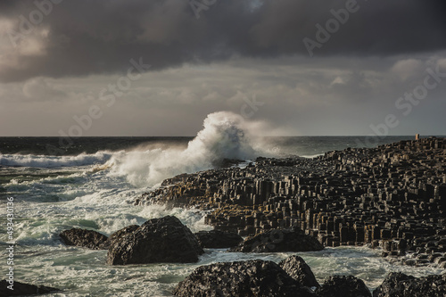 Rough ocean waves smashing on hexagonal rocks at the giant 's causeway on a murky day. Hexagon - shaped stones with a sea wave hitting the cliff convey a strong impact or major, big effect concept photo
