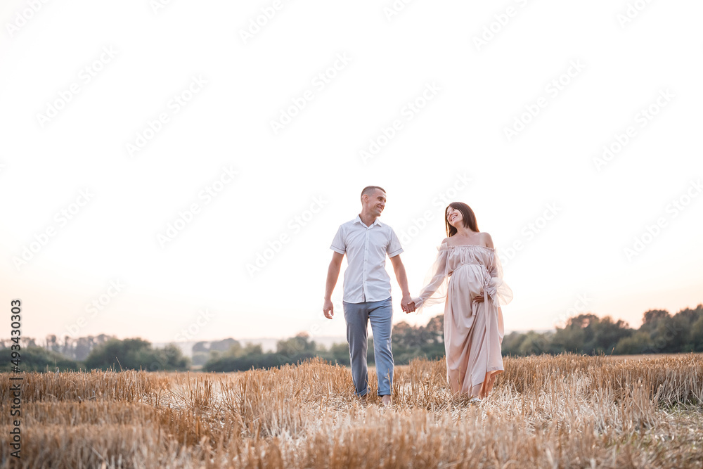 A young pregnant woman with her husband, a happy beautiful couple hugging on a golden field in the countryside. Family relationships. Future parents