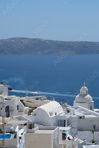 View of the whitewashed picturesque church, villas of Fira Santorini and a ferry boat arriving at the port of Athinios in
