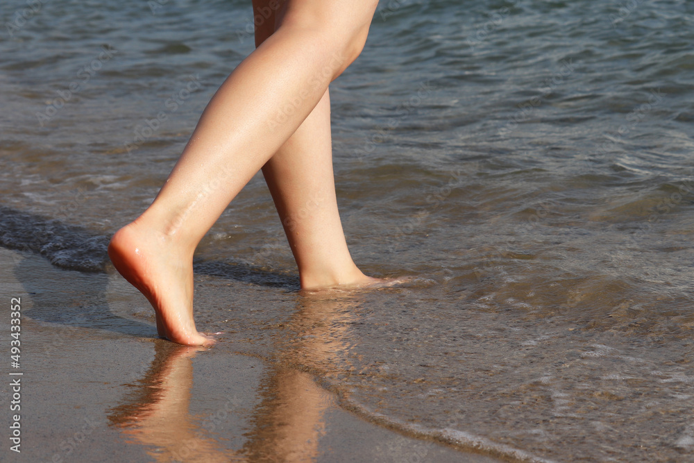 Barefoot girl running by the sand in the sea waves. Naked female legs in water, beach vacation Barefoot girl running by the sand in the sea waves. Naked female legs in water, beach vacation