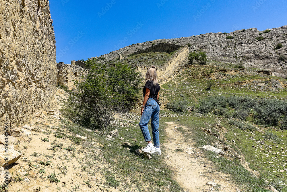 A girl against the background of the Gunib fortress. A protective wall. Russia, Dagestan. June 2021.