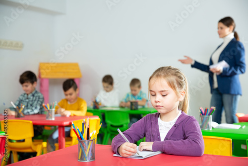Cute preteen girl studying in classroom on background with classmates and teacher. High quality photo